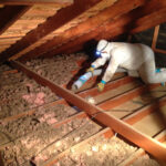 A man in white suit working on the inside of an attic.