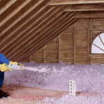 A man spraying the attic with pink foam.